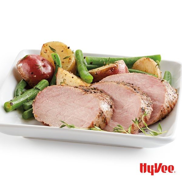 Sliced pork, fresh green beans, halved potatoes, and fresh thyme on a white square plate