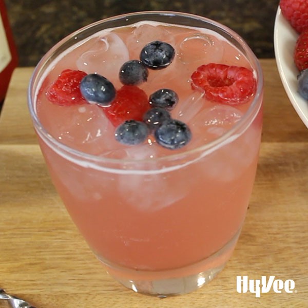 Glass filled with pink liquid and topped with whole blueberries and raspberries