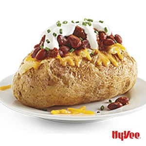 Baked potato with melted shredded cheese, chili beans, sour cream, and topped with finely chopped chives on a white plate
