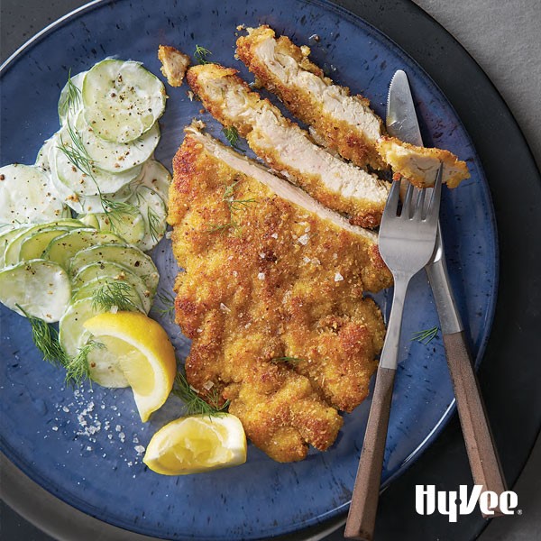 Breaded chicken breast cut on plate with cucumber salad