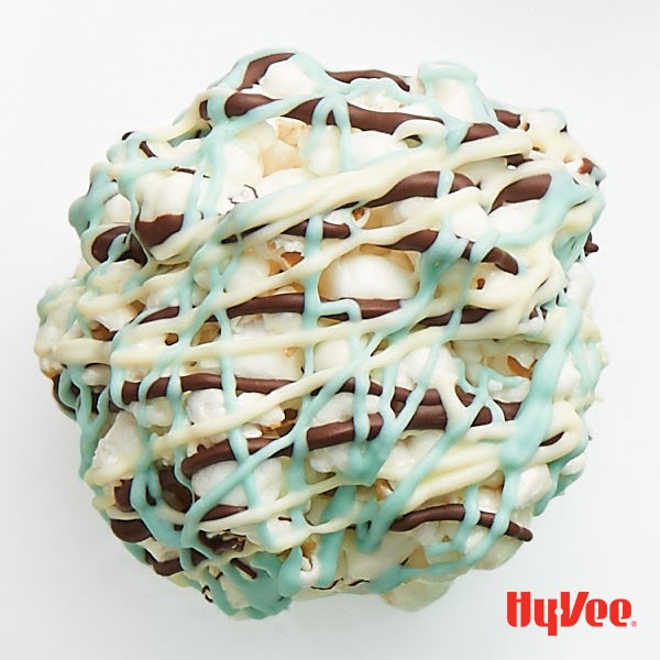 White popcorn ball drizzled with white and milk chocolate and blue-colored white chocolate