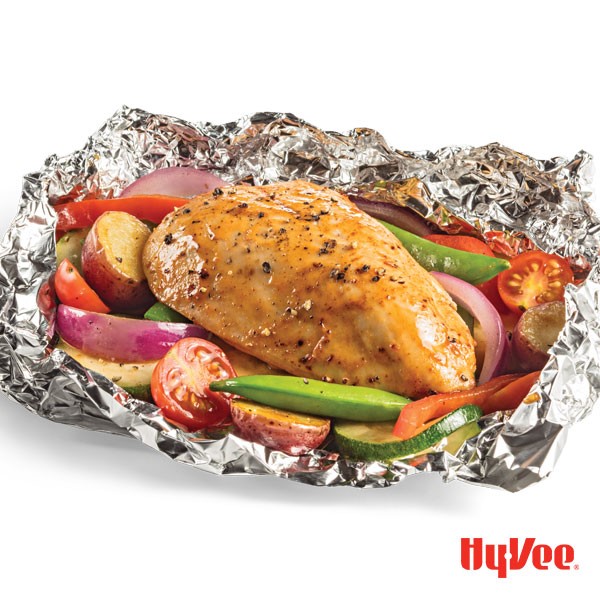 Foil packet filled with sugar snap peas, halved tomatoes and red potatoes, red pepper strips and chicken breast