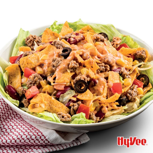 Bowl of corn chip chili salad topped with ground beef, beans, cheese, onion, black olives and tomatoes