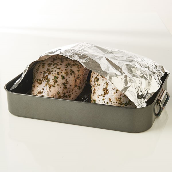 Covering raw seasoned turkey breasts in roasting pan with aluminum foil