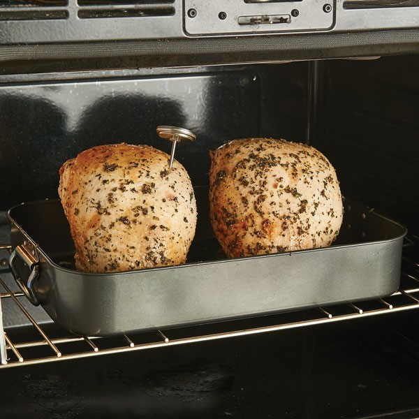 Two turkey breasts in roasting pan in oven with meat thermometer attached