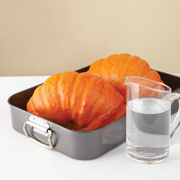 Halved pumpkins in roasting pan next to pitcher of water