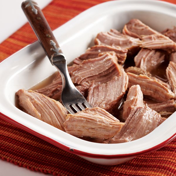 Shaved pork roast in casserole dish with fork