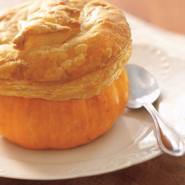 Pumpkin bowl topped with puff pastry on white plate with spoon