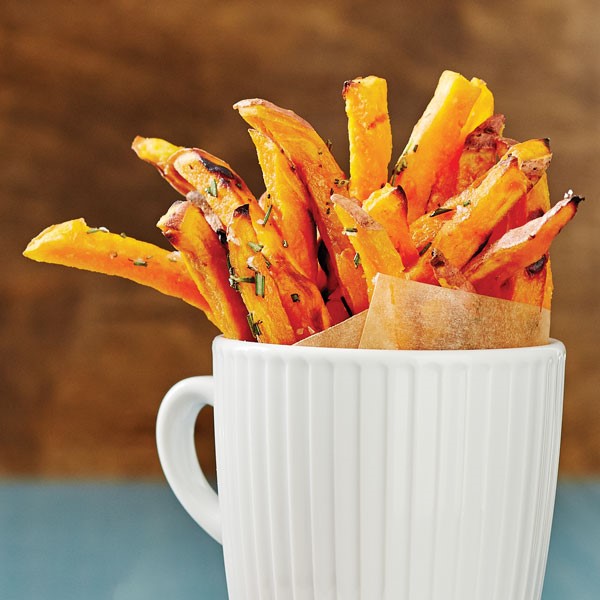 White mug filled with baked sweet potato fries garnished with fresh herbs