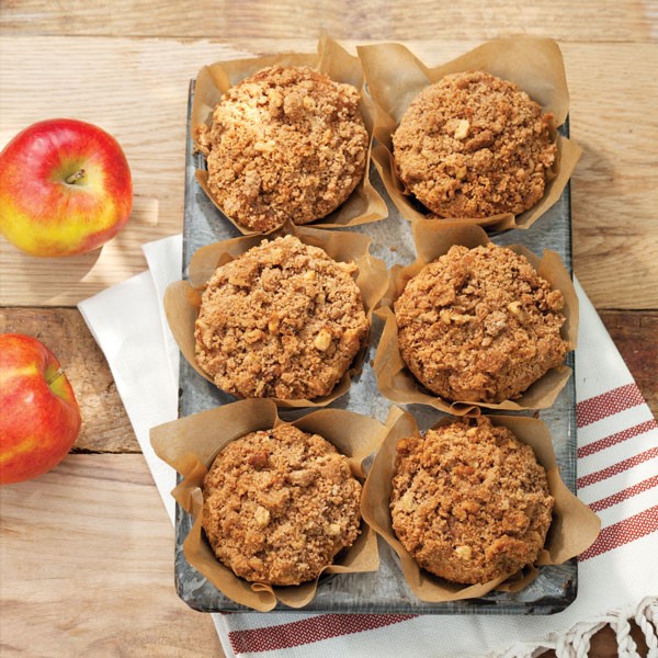 Apple muffins in tin with crumble on top surrounded by fresh apples