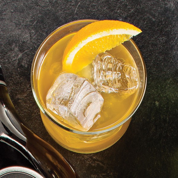 Cocktail glass filled with ice cubes, orange cocktail, and an orange wedge for garnish