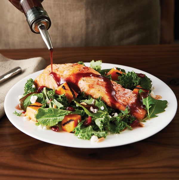 Plate of salad topped with salmon and sweet pototo wedges and drizzled with balsamic vinaigrette