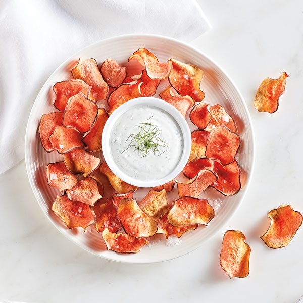 Plate of baked sweet potato chips surrounding a bowl of dill dip