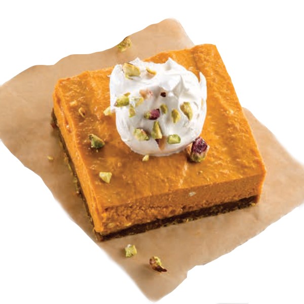 Pumpkin bar on parchment paper, topped with whipped topping and crushed pistachios 