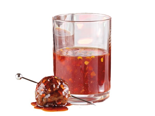 Skewered meatball coated in barbecue sauce next to cup of barbecue sauce