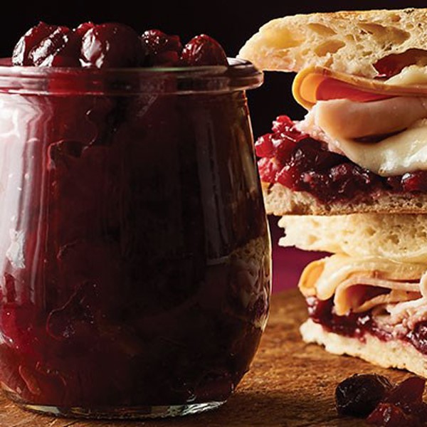 Cranberry-apple chutney next to stacked sandwiches on wooden board