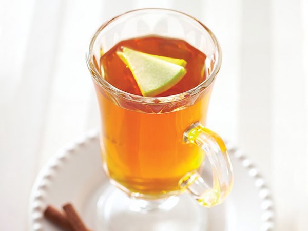 Glass of apple cider topped with apple slices and served with cinnamon sticks