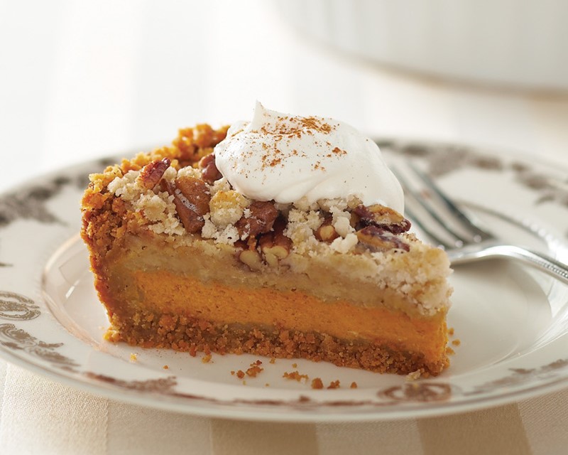 Slice of pumpkin pecan layer pie, topped with whipped topping and cinnamon on a plate