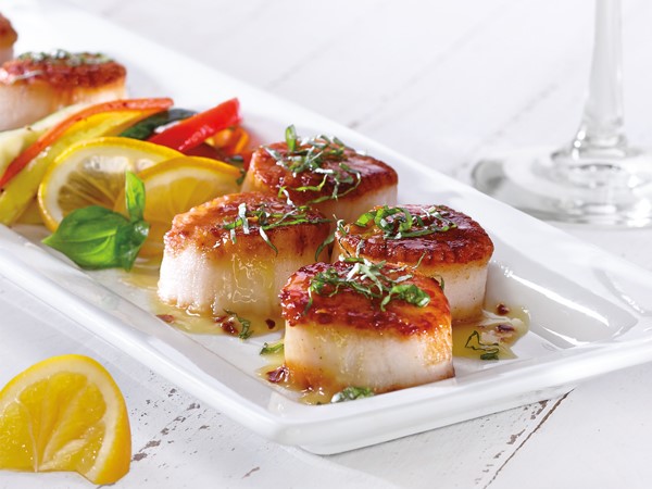 Platter of seared scallops, garnished with fresh herbs and served with vegetables and lemon slices